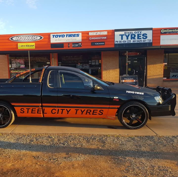 The Steel City Tyres ute, black with an orange side panel, parked outside the shop