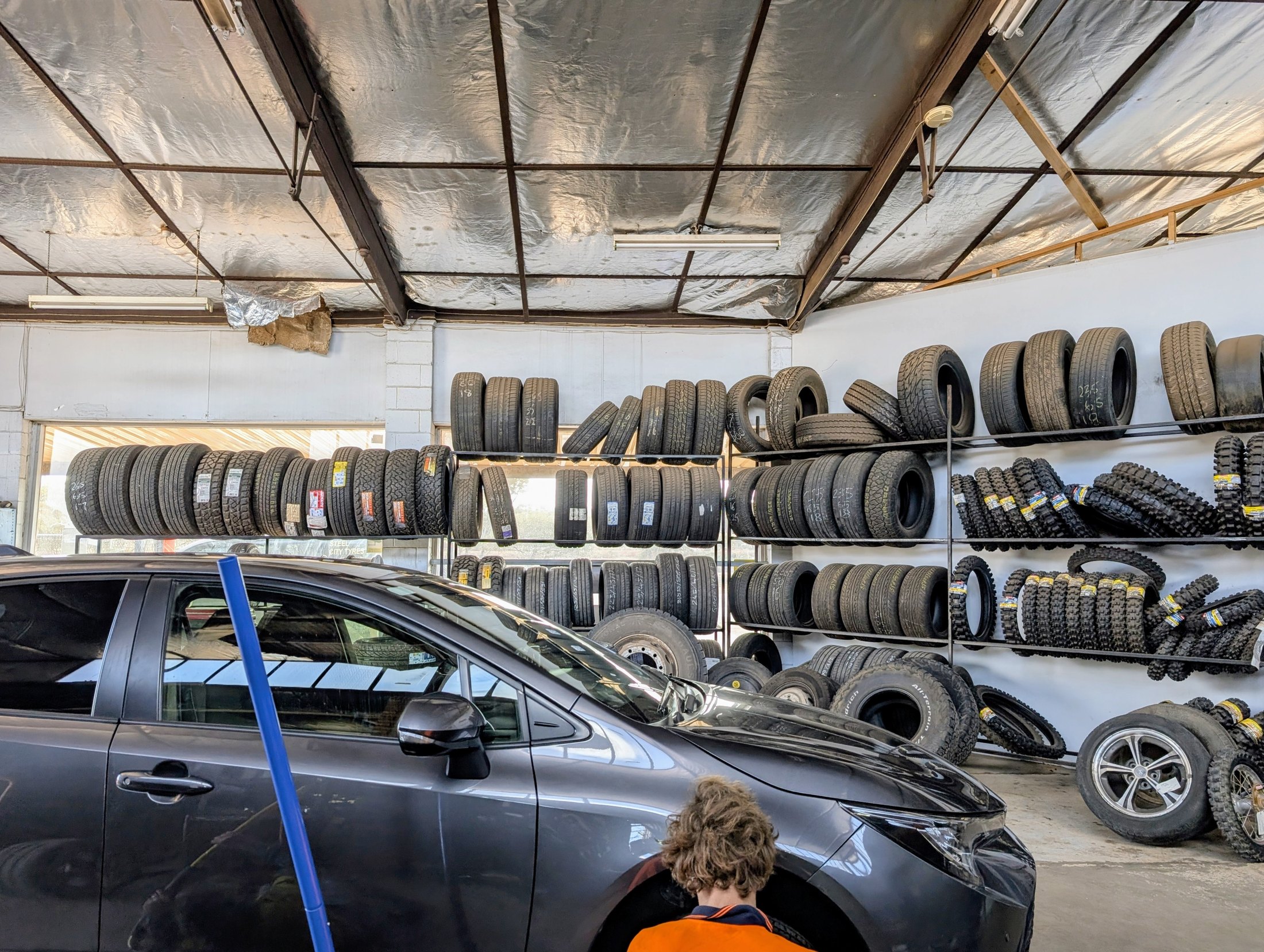 A technician fitting a wheel to a car inside the Steel City Tyres workshop, in front of racked tyres